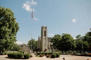 This picture portrays the College of the Ozarks chapel on a sunny day. To the left of the chapel stands an American flag, while green trees surround the scene, highlighting the beauty of the campus.